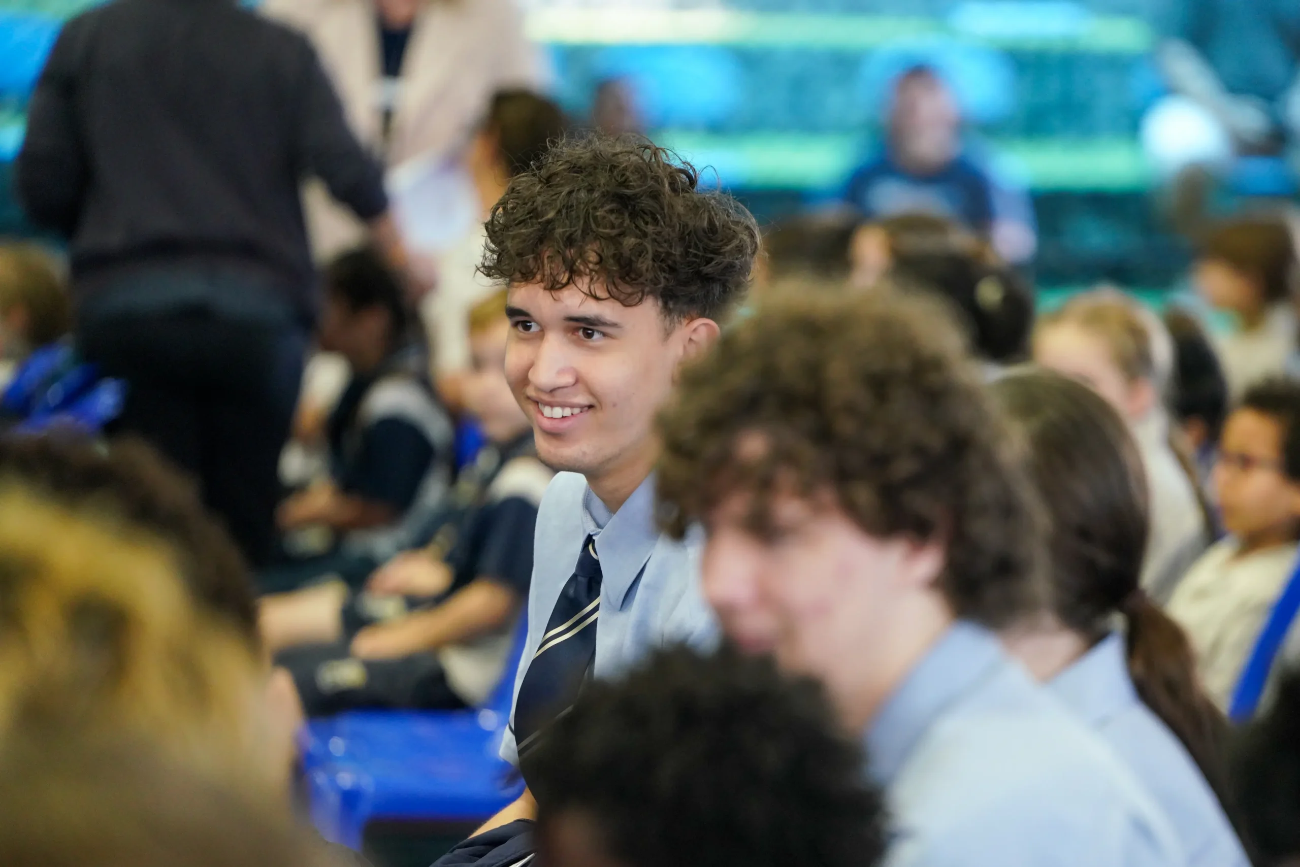 Teen sitting in a chair at a ceremony smiling at his friend.
