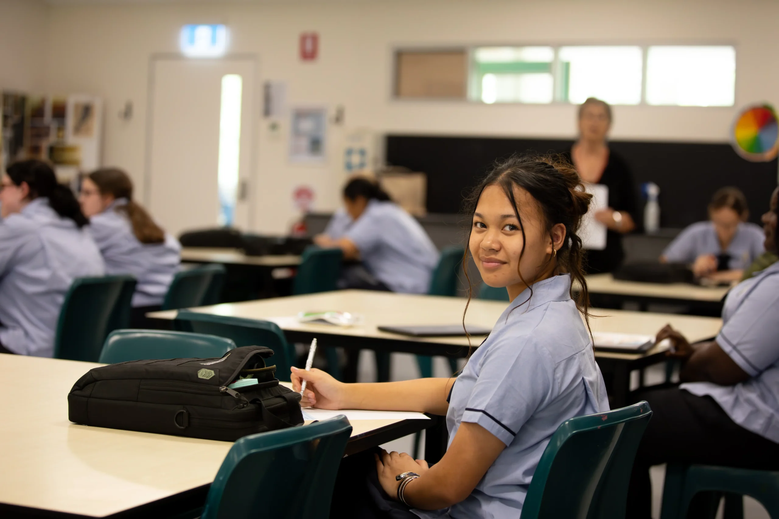 Teen sitting in a chair at a ceremony smiling at his friend.